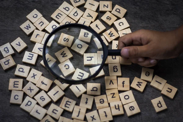 English alphabet made of square wooden tiles with the English alphabet scattered on table background. The concept of thinking development, grammar. Magnifier placed on English letters