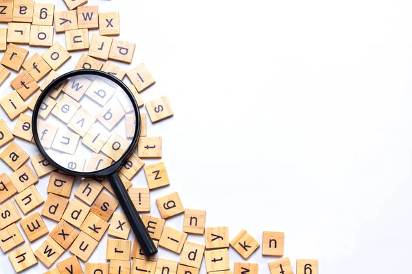 English alphabet made of square wooden tiles with the English alphabet scattered on white background. The concept of thinking development, grammar. Magnifier placed on English letters