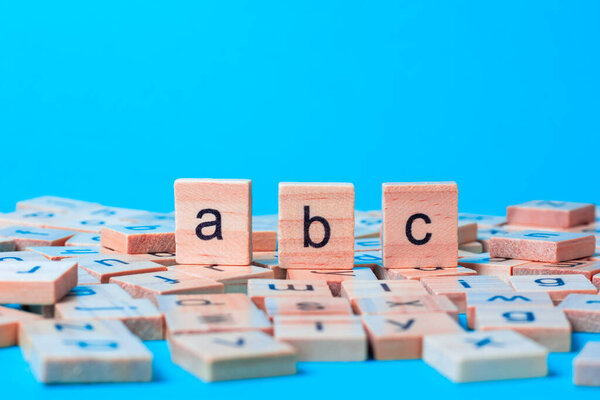English alphabet made of square wooden tiles with the English alphabet scattered on blue background. The concept of thinking development, grammar