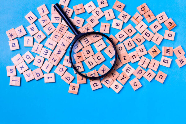 English alphabet made of square wooden tiles with the English alphabet scattered on blue background. The concept of thinking development, grammar