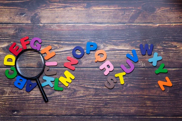 Multicolored English letters spread on the wooden floor. Magnifier and English Alphabet with English Learning Concepts, The concept of thinking development, grammar