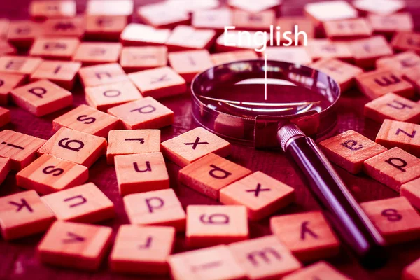 テーブルの上に英語のアルファベットが散乱した正方形の木製のタイルで作られた英語のアルファベット 思考の発達 文法の概念 英語の文字に置かれた拡大鏡 — ストック写真