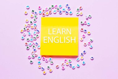 İngilizce öğrenme kavramını temsil eden açık pembe arkaplan üzerine dağılmış İngilizce harfler.