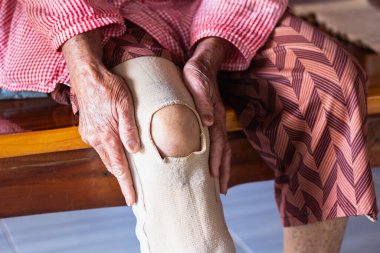 Yaşlı bir kadın dizini acıdan tutarak oturdu..