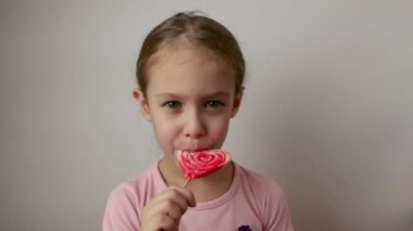 Tatlı bir kız büyük kırmızı bir lolipop yalıyor. İzole edilmiş beyaz arkaplan.