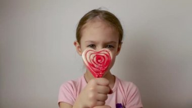 A cute little girl is holding a heart-shaped candy cane in her hands. Valentines Day. Delicious dessert. Isolated white background.