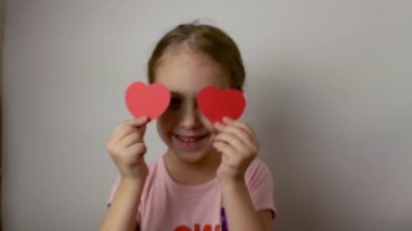 Cute little girl plays with postcards in the form of red hearts. Valentines Day. Congratulations on the holiday. Isolated white background