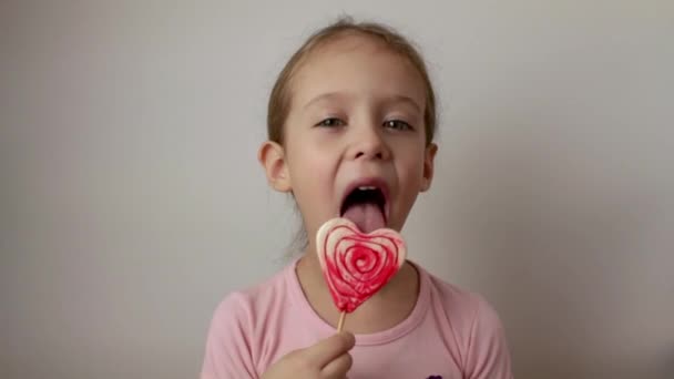 Милая Маленькая Девочка Лижет Большой Красный Белый Леденец Форме Сердца — стоковое видео