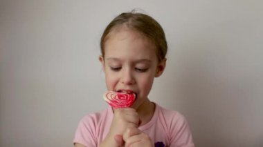 A cute little girl eats a heart-shaped lollipop dessert. Valentines Day. Delicious dessert. Isolated white background.