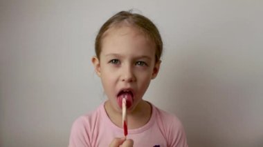 A cute little girl licks a heart-shaped lollipop. Delicious dessert. Isolated white background.