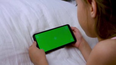 Çocuk yatakta bir cep telefonunu izliyor. Krom yeşil ekran. Telefondaki oyun ya da çizgi film. Reenka çevrimiçi ders çalışıyor ve dersleri geliştiriyor. Video.