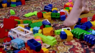 Çocuk dağınık küplerin arasında yürüyor. Çocuk odasındaki dağınıklık. Dağılmış inşaatçı. Hafta sonu çocukları evde. Çocuk gelişimi. Bahar temizliği. Bacaklarını kapat..