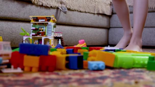 子供は散乱した立方体の間を歩く 子供部屋でメス 散乱コンストラクタ 自宅で週末の子供たち 子供の発達 春の掃除 足を閉じて — ストック動画