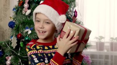 Noel şenliği havası. Noel Baba şapkalı coşkulu küçük bir kız kırmızı bir fiyonkla karışık bir hediye kutusuna dokunup sallıyor..