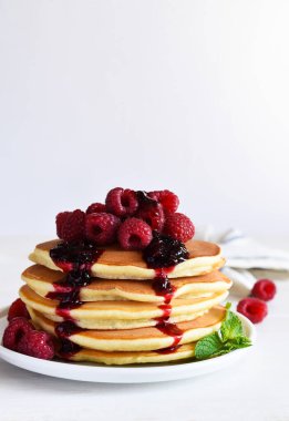 Beyaz arka planda kahvaltıda ahududu ve reçelli ev yapımı krepler.