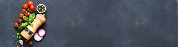 Biber öğütücü, fesleğen, baharat ve sebzeler siyah mutfak masasında yazılı. Yiyecek malzemeleri..