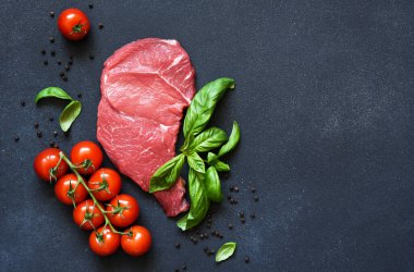 Çiğ et, domatesli biftek ve siyah arka planda fesleğen. Metin için yer.