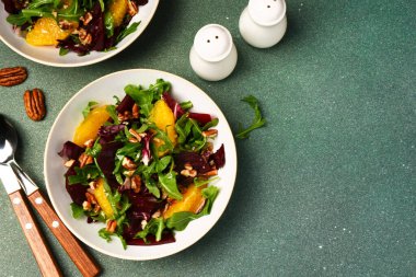 Salad with arugula, orange and beet in a plate on a green background clipart