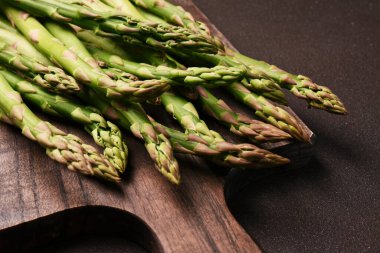 Koyu arkaplanda tahta üzerinde taze çiğ kuşkonmaz.