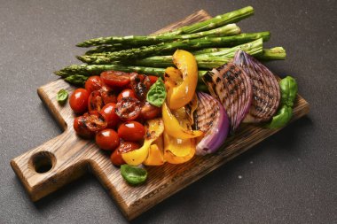 Izgara sebzeler: Kuşkonmaz, domates, ahşap tahtada soğan siyah arka planda.