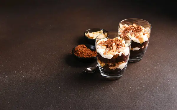Chocolate cake in a glass with vanilla cream and almonds. A portion of dessert in a glass on a dark background.