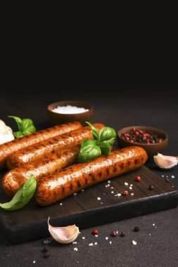 Koyu arkaplanda ahşap bir tahtada baharatlı ızgara sosis.