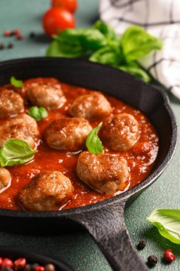 Domates soslu köfte ve yeşil arka planda dökme demir tavada fesleğen.