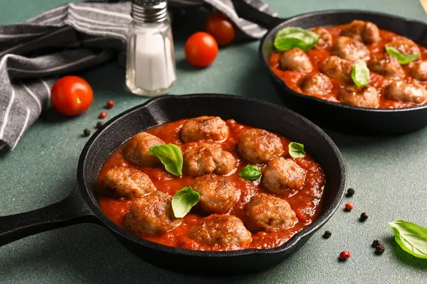 Domates soslu köfte ve yeşil arka planda dökme demir tavada fesleğen.