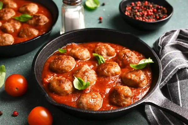 Meat balls in tomato sauce with basil in a cast iron frying pan on a green background