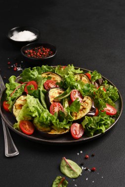 Izgara domatesli marul yaprakları ve koyu bir arka planda patlıcan.