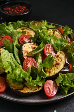 Izgara domatesli marul yaprakları ve koyu bir arka planda patlıcan.