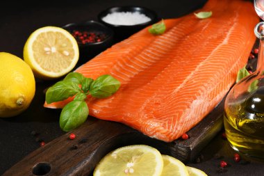 Koyu bir zemin üzerinde, limon ve baharatlı ahşap bir tahtada somon parçaları.