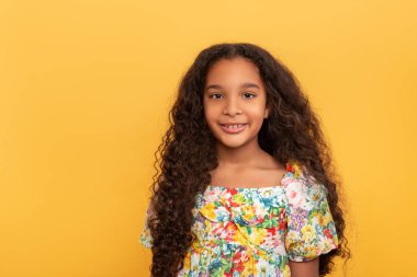Half length portrait of a dark skinned young girl with long curly hair  on a yellow background