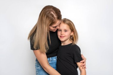 Aynı siyah gömlek ve kotu giyen mutlu anne ve kızın yarım boy portresi stüdyoda beyaz bir arka planda birbirlerine şefkatle bakıyorlar.