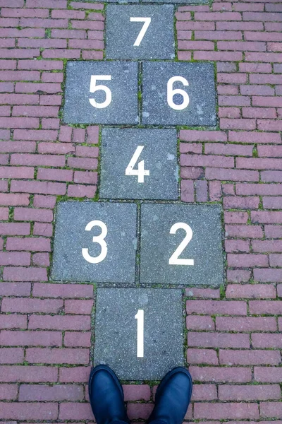Squares with numbers are drawn on paving slabs - a children\'s hopscotch game. Near the boots of an adult who remembered childhood.