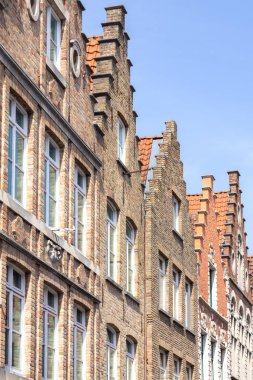 Belçika 'nın Bruges kentindeki ortaçağ tuğlalı evlerinin mimarisi mavi gökyüzüne karşı dizilmiş..