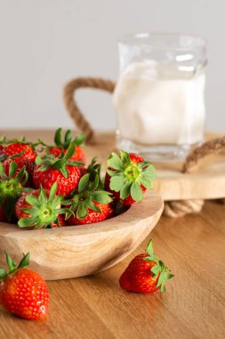 Tahta bir vazoda çilek, sütlü bir bardağın yanında jüt saplı ahşap bir tepside.