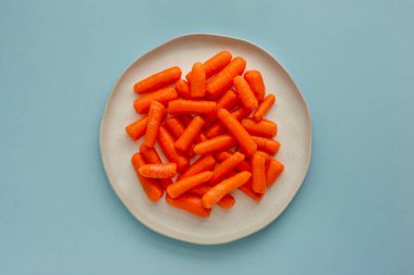 Birçok küçük taze havuç mavi arka planda açık seramik bir tabakta uzanır, üst manzara. Sağlıklı yaşam kavramı.