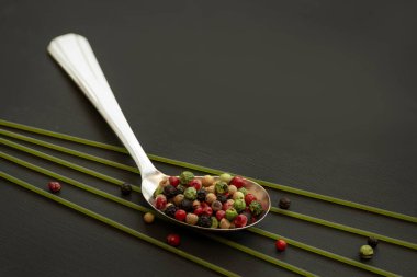 Farklı türde biber ve renklerde sıra dışı bir kaşık siyah masada ıspanaklı yeşil spagetti ile yatıyor..