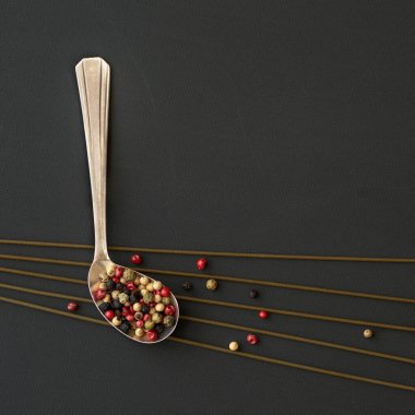 Spagetti ve sıradışı kaşık. Farklı türde karabiberler ve siyah masanın üzerindeki renkler.