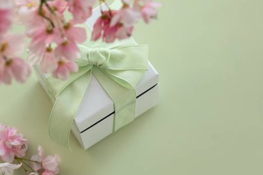 Yeşil arka planda yeşil fiyonklu beyaz hediye kutusu fotokopi alanı ve pembe kiraz çiçekleri.