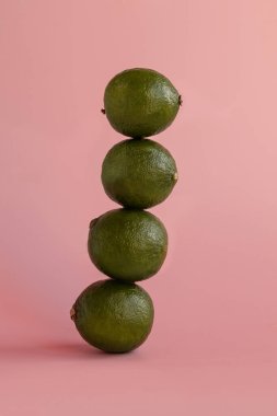 Birkaç kireç meyvesi üst üste durarak pembe arka planda bir kule oluşturur..