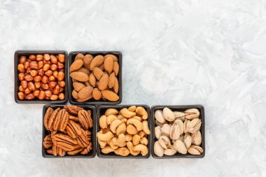 Siyah kare seramik kaselerde fındık çeşitleri. Gri desenli arka plan, fotokopi alanı, üst görünüm. Sağlıklı beslenme ve sağlıklı yaşam kavramı,