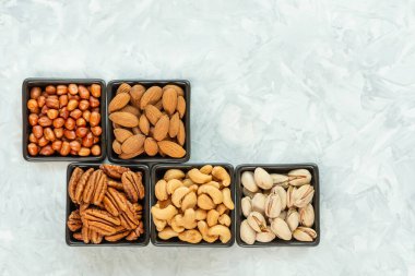 Siyah kare seramik kaselerde fındık çeşitleri. Gri desenli arka plan, fotokopi alanı, üst görünüm. Sağlıklı beslenme ve sağlıklı yaşam kavramı,