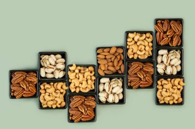 Siyah kare seramik kâselerdeki fındık çeşitleri. Fotokopi alanı ve üst görünümü olan yeşil bir zemin üzerinde. Sağlıklı beslenme ve sağlıklı yaşam kavramı.