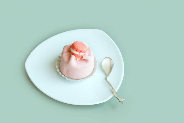 Крупный план розового торта с декором, лежащего на треугольной пластине с декоративной ложкой на зеленом фоне, вид сверху. 