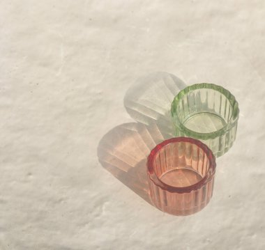 Bej desenli arka planda güneş ışığının yansımasıyla desenli iki cam bardak.