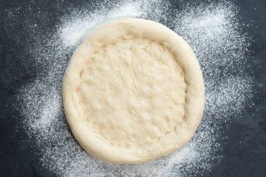 Karanlık bir masanın üzerinde duran pizza hamurunun yakın plan çekimi.