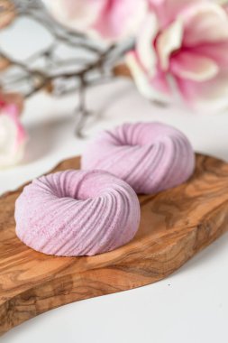 Beyaz bir masanın üzerindeki ahşap dokuma tahtasının üzerinde iki tane köpük pembesi. Arkasında bir manolya filizi yatıyor.