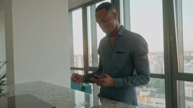 Genç siyahi bir adam pahalı bir dairede duran kartvizitinden telefonuna kadar her türlü bilgiyi yazar. Genç işadamı dairesinde kartvizit okuyor. Yüksek kalite 4k görüntü